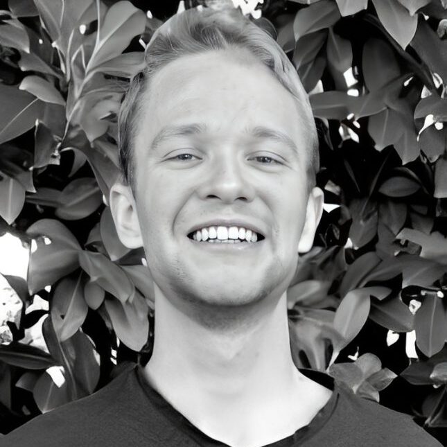 Smiling person in front of leafy background.