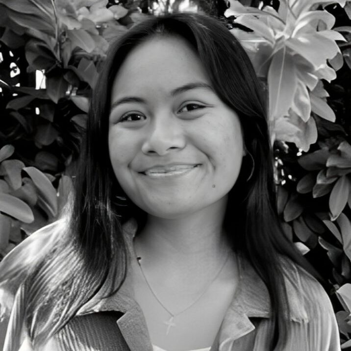 Smiling person in front of leafy background.