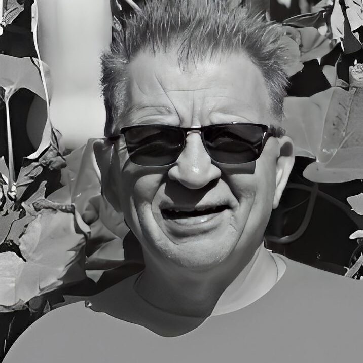Man wearing sunglasses, smiling outdoors.