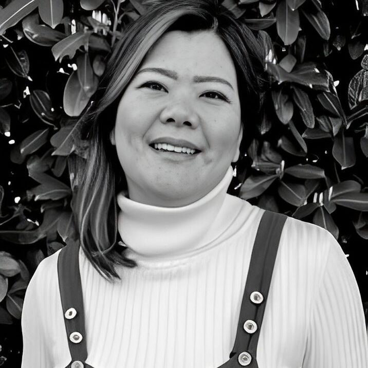 Smiling woman in front of leafy background.