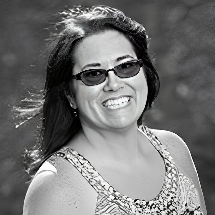 Smiling woman wearing sunglasses outdoors, black-and-white.