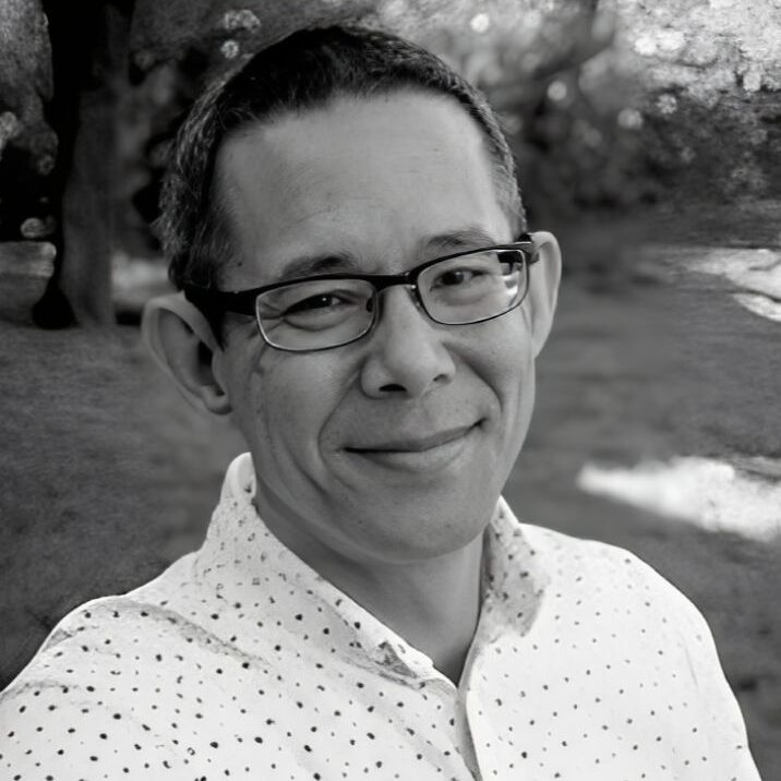 Smiling person outdoors, wearing glasses and shirt.