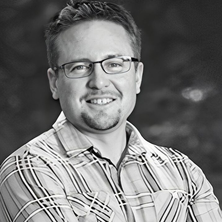 Man smiling, wearing glasses and plaid shirt.