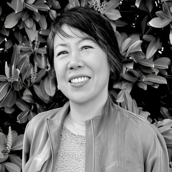 Smiling person in front of leafy background.