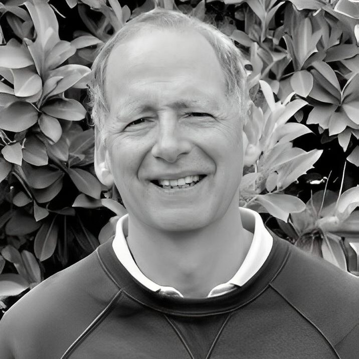 Smiling man in front of leafy background.