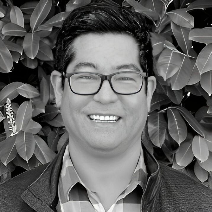 Smiling person in front of leafy background.