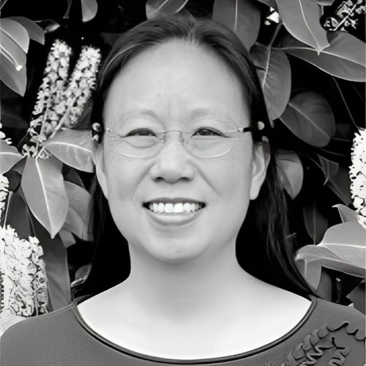 Smiling person in front of leafy background.